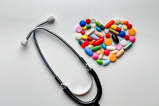 Health themes: Large group of assorted capsules and pills making a heart shape with a stethoscope on white background