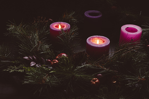 Rustic advent wreath in a dark room with two purple candles lit with copy space for the second week of advent