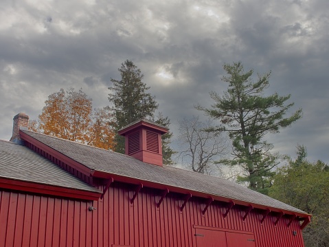 Stormy skies above the roof line of a red agricultural barn in the Berkshires. A agricultural design element with copy space.