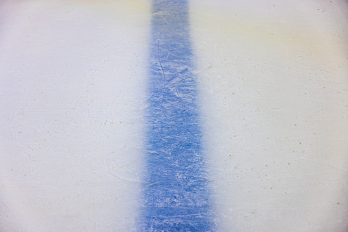 Close-up view of blue dividing line beneath intricately patterned surface of ice rink. Texture or background option.
