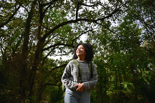 multiracial woman with curly hair standing in a woodland and admiring the nature.