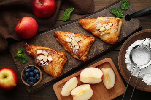 Fresh tasty puff pastry with sugar powder, mint, blueberries and apples served on wooden table, flat lay