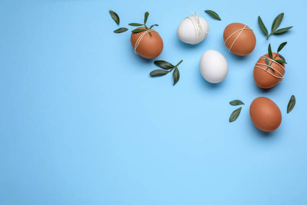 istock Beautifully decorated Easter eggs and green leaves on light blue background, flat lay. Space for text 1779065292