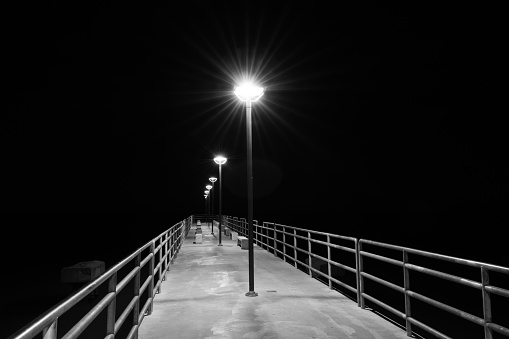 Black and white long exposure shot of streetlamps glowing on pier at night.
