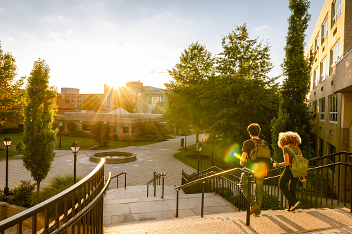 Rear view of two university students walk down campus stairs at sunset
