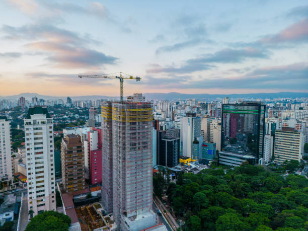 Building under construction with crane, green area and a mirrored building