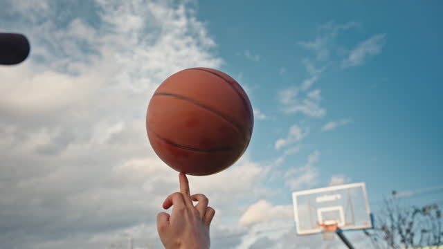 SLO MO Close-Up of Crop Boy Spinning Basketball on Finger at Court Under Blue Cloudy Sky