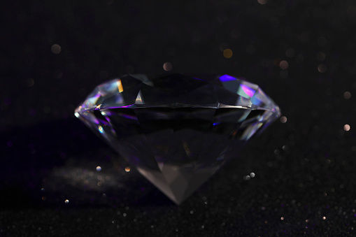 Beautiful dazzling diamond on black glitter surface, closeup