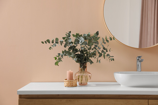 Stylish mirror, eucalyptus branches and vessel sink in modern bathroom. Interior design
