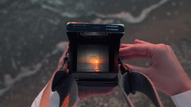 View through old film camera viewfinder. Female hands holding retro analogue tlr medium format 120 mm camera and taking picture of the sea on the beach at sunset