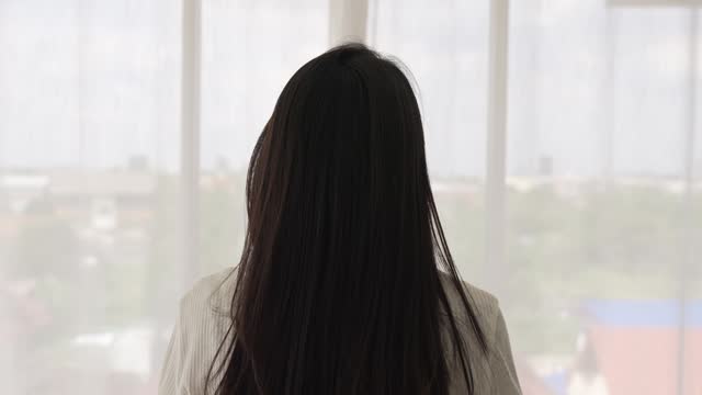 Asian woman styling her own hair by hand in bedroom, lifestyle concepts, slow motion clip.