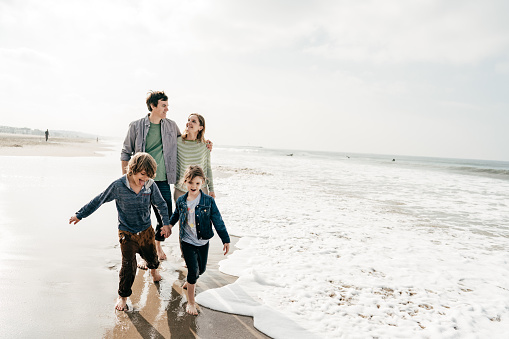 Parents Running Along Beach With Children On Summer Vacation