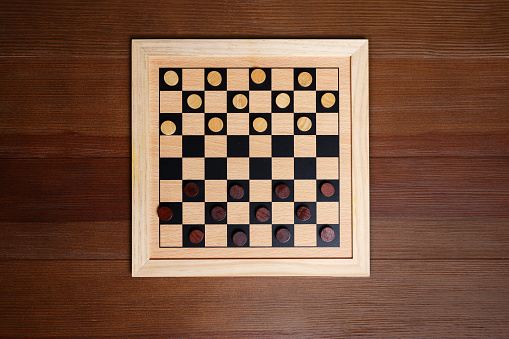 Checkerboard with game pieces on wooden table, top view