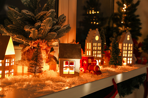 Christmas atmosphere. Many beautiful glowing houses on window sill indoors