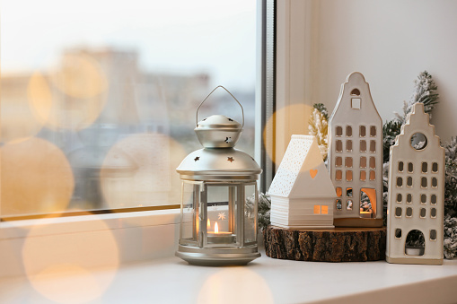 Beautiful house shaped candle holders and Christmas decor on windowsill indoors, space for text. Bokeh effect