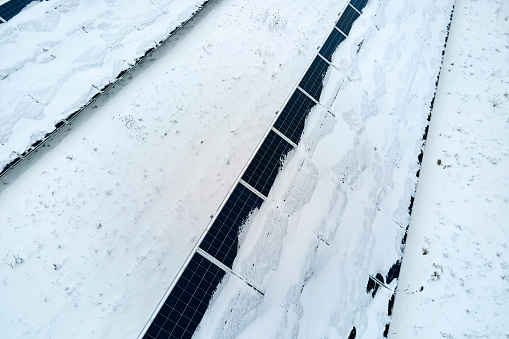 Aerial view of snow covered sustainable electric power plant with rows of solar photovoltaic panels for producing clean electrical energy. Low effectivity of renewable electricity in northern winter.