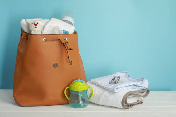 istock Mother's bag with baby's stuff on white wooden table against light blue background 1779263844