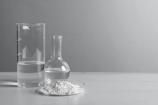 Petri dish with calcium carbonate powder and laboratory glassware on white table. Space for text