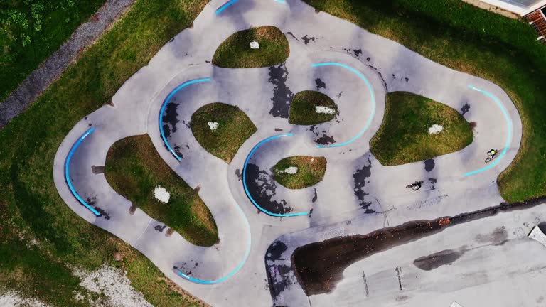 AERIAL Directly Above Drone Shot of Sister And Brother Riding Bicycles on Pump Track in Park