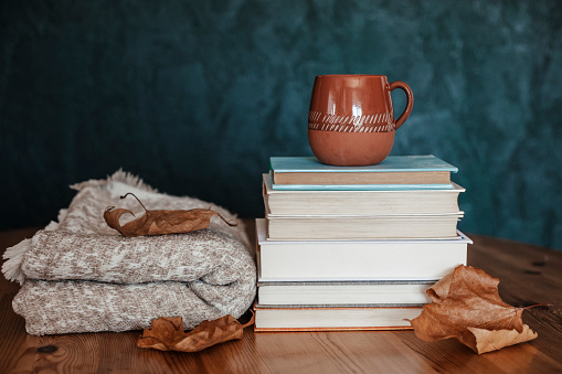 Composition with a stack of books, hot beverage in the mug and warm blanket. Cozy reading scene for cold weather with cup of coffee