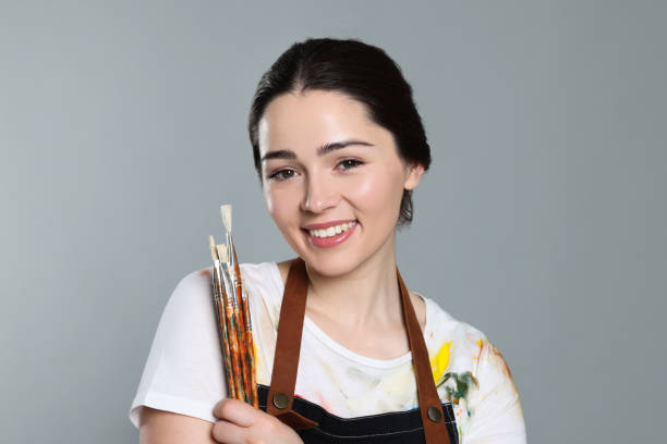 istock Woman with paintbrushes on grey background. Young artist 1779317526