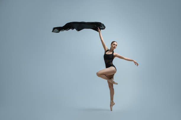 Graceful young ballerina practicing dance moves with black veil on grey background. Space for text