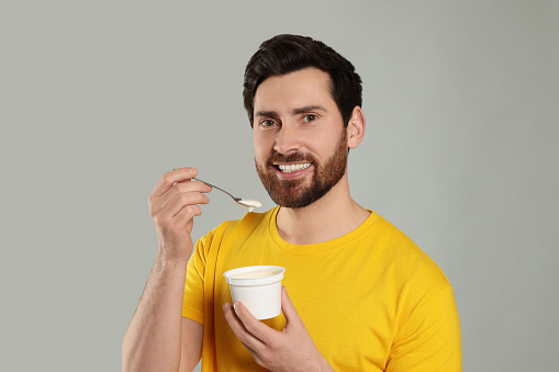 Handsome man with delicious yogurt and spoon on light grey background