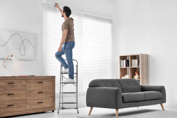 hombre en escalera plegable de metal instalando persianas en casa. espacio para el texto - escaleras de aluminio fotografías e imágenes de stock