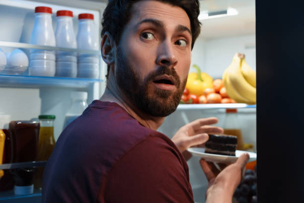 istock Man taking plate with cake from refrigerator in kitchen at night. Bad habit 1779350853