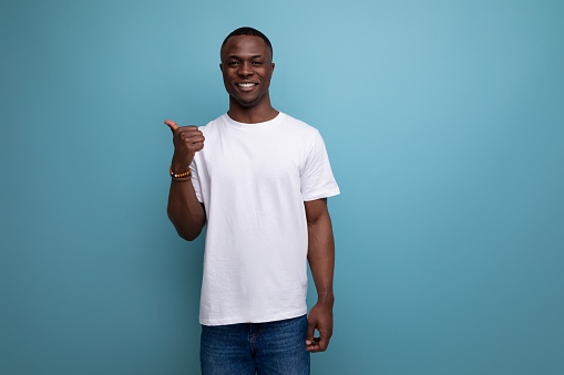 handsome 30s african man with short haircut in white t-shirt shows his hand towards space.