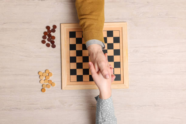 istock Playing checkers. Partners shaking hands after match at white wooden table, top view 1779369948