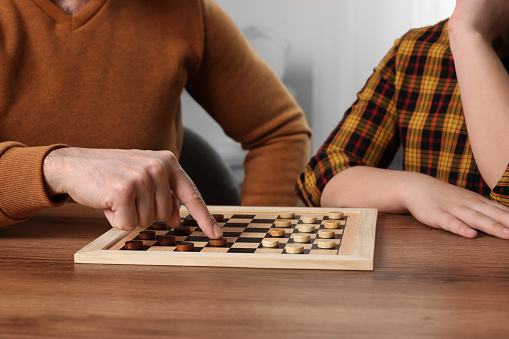 Father playing checkers with his son at table in room, closeup