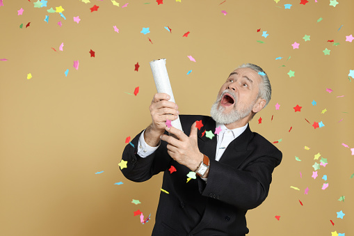 Emotional man blowing up party popper on beige background