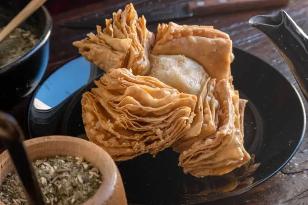 Argentinian pastelito next to a kettle, a mate and yerba mate.