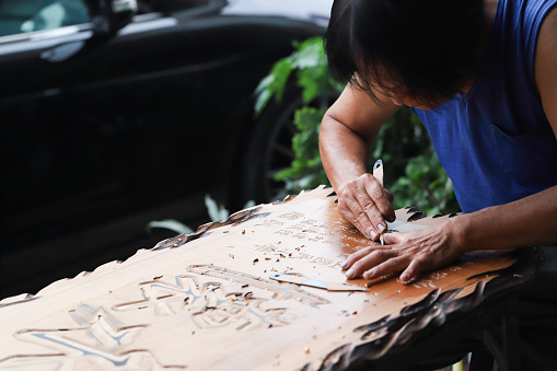 The woodcarving master is carving a plaque. 
He carved Chinese characters on the plaque. Handmade woodcarving is one of Taiwan's traditional products. It is gradually declining, and handcarving is gradually being replaced by machine carving. The content of the plaque is some blessings and gratitude, wishing the store prosperity or safety.
