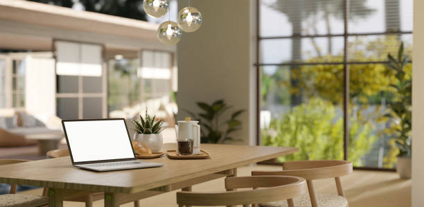 istock A white-screen laptop mockup on a wooden dining table in a spacious modern Scandinavian dining room. 1779479004