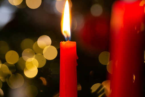 Red candles.Burning candles on bokeh background.Christmas festive background with red burning candles and bokeh garland.cozy festive atmosphere