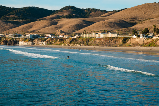 Pismo beach hills with  cliffs, wide sandy beach, dark blue ocean, and silhouette of a town in the background at sunset, California Central Coast