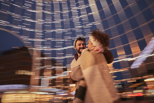 Cheerful couple having fun inside of Christmas decoration on the city street at night. Blurred motion.