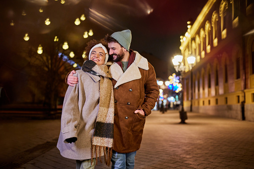 Young happy couple walking embraced during Christmas night on the city street.