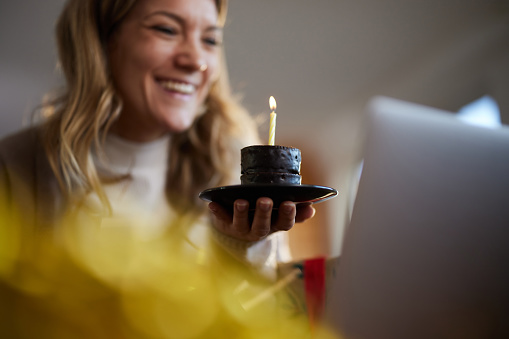 Close up of happy woman having fun while celebrating her Birthday with someone through video call at home.