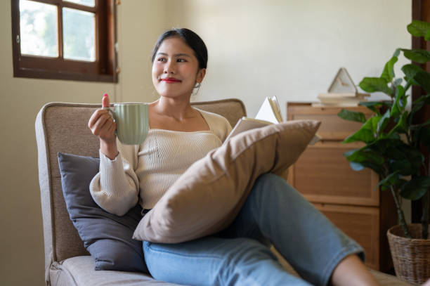 istock A charming Asian woman enjoys her morning coffee while reading a book on a couch. 1779585361