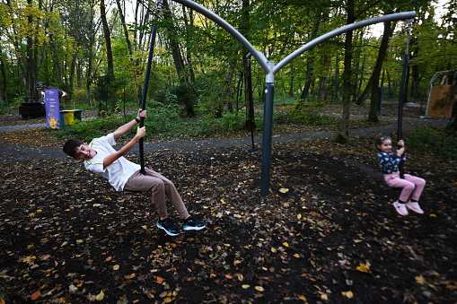 Boy swinging on a swing in an autumn park with his little sister.