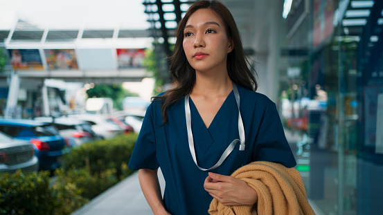 Positive young Asian healthcare staff doctor or nurse in scrubs uniform standing and walking at corridor, Medical technician with activities in daily life, Woman lifestyle in scrubs