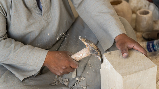 A man traditionally creating Egyptian sculptures by hand with stone chips flying off