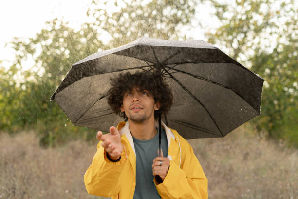 istock Happy arabic young man with umbrella under the autumn shower. Guy enjoying rainfall on the nature outdoors. Walk in the park. 1779656830
