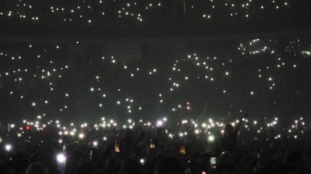 Fan people wave cell phone flashlight at music concert stadium. Crowd atmosphere Many fun people lift hands up hold cell phone flash light. Happy fans crowd wave flashlights. Epic live music concert atmosphere. Big k pop arena. Cool night fest. A lot of joy men hang out stadium. mobile phone lights up stock pictures, royalty-free photos & images