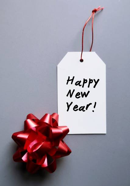 istock Red gift bow and white gift tag with hand written text HAPPY NEW YEAR - on gray background , concept of new year holiday gift for love ones 1779730065