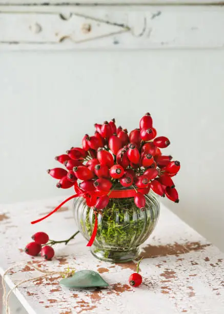 Photo of Beautiful bouquet of rose hips in vintage glass vase as autumn decoration.