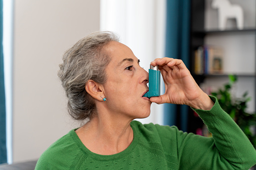 Senior woman using asthma inhaler at home